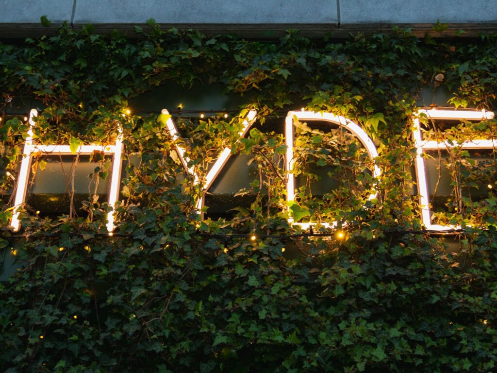 Illuminated “HYDE” signage glowing in warm white neon lights, partially covered by lush green ivy on an exterior wall.